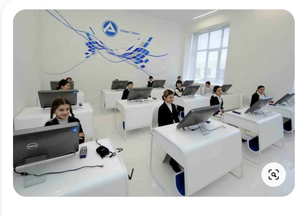 A bland white classroom with individual students sitting at individual desks with a laptop each. They are smiling though.